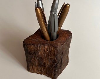 May include: A wooden pen holder made from a tree trunk with a natural bark finish. The holder is filled with gold and silver pens.
