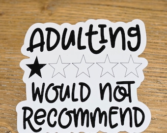 May include: A white sticker with black text that reads "Adulting Would Not Recommend." The word "Adulting" is above a row of five stars, one filled in. The sticker is on a wooden surface.