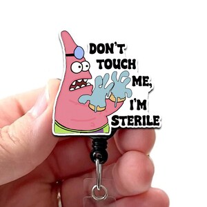 May include: A pink, cartoon Patrick Star badge reel with the text "DON'T TOUCH ME, I'M STERILE." The reel features a black cord and a clear plastic clip. The design includes a doctor's hat and gloves.