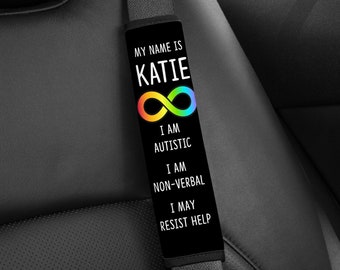 May include: Black seatbelt cover with the text "MY NAME IS KATIE" and an infinity symbol in rainbow colors. Below the symbol, the text reads "I AM AUTISTIC, I AM NON-VERBAL, I MAY RESIST HELP."