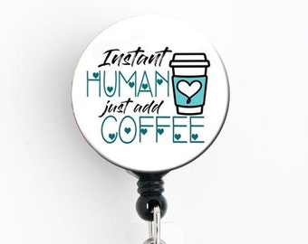May include: White retractable badge holder with a black strap and a round, white badge with the text "Instant Human just add Coffee" and a blue and white coffee cup graphic.