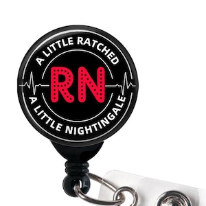 May include: A black and white badge reel with the text "A Little Ratched, A Little Nightingale" encircling a red "RN" with a heartbeat graphic. The reel has a clear plastic strap and a metal clip.