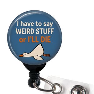 May include: A blue badge reel with the text "I have to say WEIRD STUFF or I'LL DIE" and a cartoon goose. The reel has a black base, a metal clip, and a clear plastic strap with a snap closure.