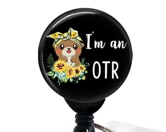 May include: Black and white badge reel with a black button and a clear plastic strap. The badge holder features a cartoon otter wearing a yellow bandana and surrounded by sunflowers. The text "I'm an OTR" is printed in white on the badge holder.