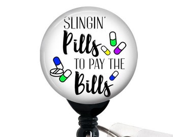 May include: White round badge holder with a black retractable cord and a clear plastic clip. The badge features a white background with black text that reads "Slingin' Pills to Pay the Bills". The text is surrounded by colorful pill illustrations.