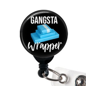 May include: A black retractable badge holder with a round button featuring a stack of blue wrapped gifts and the text "Gangsta Wrapper".
