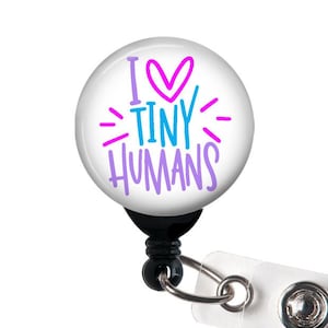 May include: A white badge reel with a round button featuring the text "I ♥ TINY HUMANS" in pink, blue, and purple lettering. The badge reel has a black retractable cord and a clear plastic clip.
