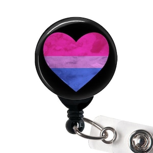 May include: A black retractable badge holder with a round, black button featuring a pink, purple, and blue heart with a watercolor effect. The heart is a symbol of the bisexual pride flag.