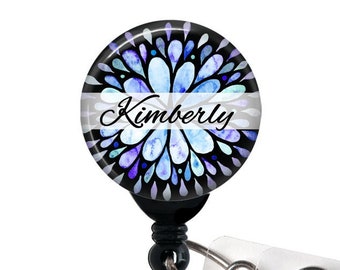 May include: A black and white retractable badge holder with a blue and purple watercolor floral design and the name "Kimberly" printed on a white banner.