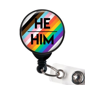 May include: A black retractable badge holder with a round, colorful button that says "HE HIM" on it. The button features a rainbow stripe design with black, brown, pink, light blue, yellow, orange, red, purple, and blue stripes.