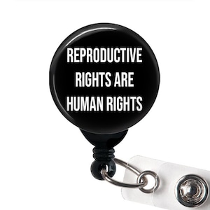 May include: Black retractable badge holder with a round black button that reads "Reproductive Rights Are Human Rights".
