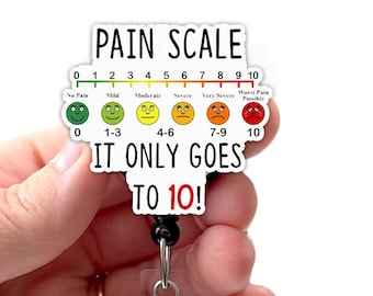 May include: A white plastic badge holder with a black retractable badge reel. The badge holder has a pain scale with a smiley face graphic for each level of pain. The text on the badge holder reads "PAIN SCALE" and "IT ONLY GOES TO 10!"
