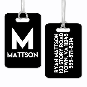 Może przedstawiać: Dwie czarne metki bagażowe z białym tekstem. Pierwsza metka ma dużą białą literę M i nazwisko Mattson. Druga metka zawiera imię i nazwisko Ryan Mattson, adres i numer telefonu.