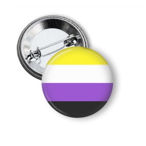 May include: A round button with a pin back featuring the non-binary pride flag. The flag has yellow, white, purple, and black horizontal stripes.