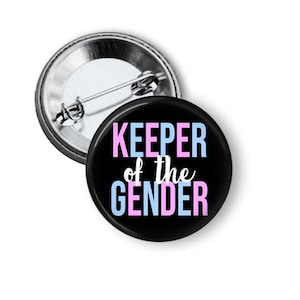 May include: A black button with the text "KEEPER of the GENDER" in white, pink, and blue lettering. The button is attached to a silver pin back.