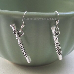 May include: Silver earrings with a flute design. The earrings are hanging from a green bowl.