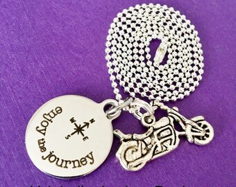 May include: Silver necklace with a round pendant that says "Enjoy the journey" with a compass design and a small motorcycle charm.