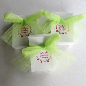 May include: Three white gift boxes with green tulle bows and a red and white circular label that says "Valebella Jewelry Designs".