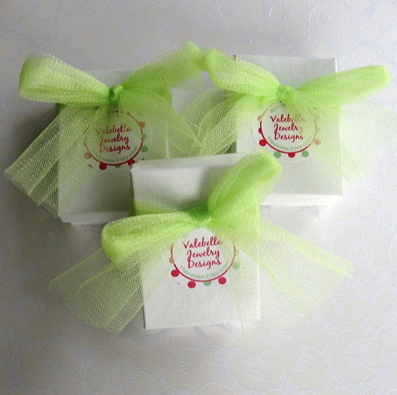 May include: Three white gift boxes with green tulle bows and a red and white circular label that says "Valebella Jewelry Designs".