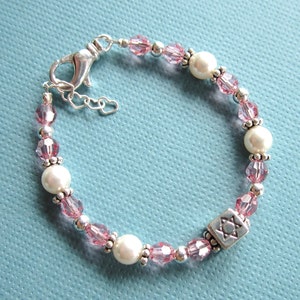 May include: A pink and white beaded bracelet with a silver Star of David charm. The bracelet is made with small pink glass beads, white pearls, and silver beads.