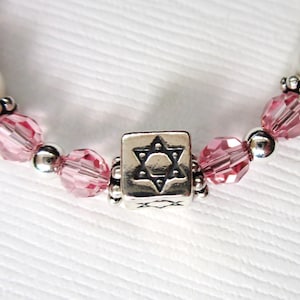 May include: A silver charm bracelet with pink crystal beads and a silver charm featuring a Star of David.