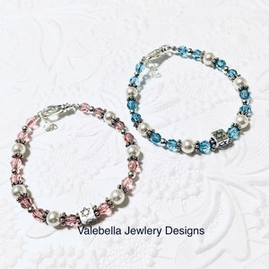 May include: Two beaded bracelets with silver clasps and charms. One bracelet has pink and white beads, the other has blue and white beads. Both charms are silver and feature a Star of David.