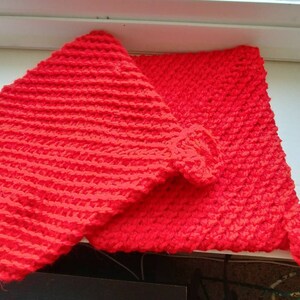 May include: Two handmade, bright red knitted items. One is a square, the other is a rectangular shape with a rounded edge. The items are made of a thick, textured yarn, and appear to be a set.