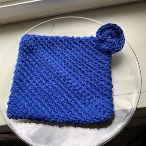 May include: A blue crocheted dishcloth with a small crocheted flower attached to one corner.