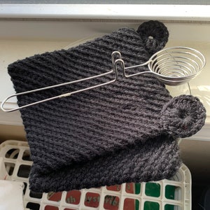 May include: A black knitted pot holder with a silver egg separator. The pot holder has a textured surface and is shaped like a mitten. The egg separator is a spiral design with a handle.