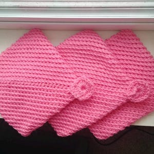 May include: Three handmade pink crochet washcloths with a textured stitch pattern. Each washcloth has a small, circular crochet flower attached. The washcloths are square and appear soft and absorbent.