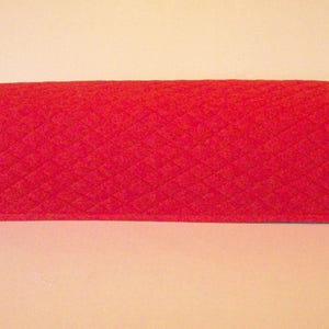 May include: A quilted, red fabric cover with a diamond pattern. The cover has a rectangular shape with rounded edges. The item is likely a cover for a kitchen appliance, such as a toaster oven or microwave.