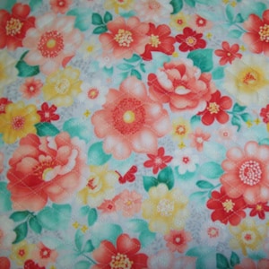 May include: Floral fabric with a quilted pattern. The design features large, coral-colored flowers with yellow centers, interspersed with smaller red and yellow blossoms. Green leaves and a light blue background complete the design.