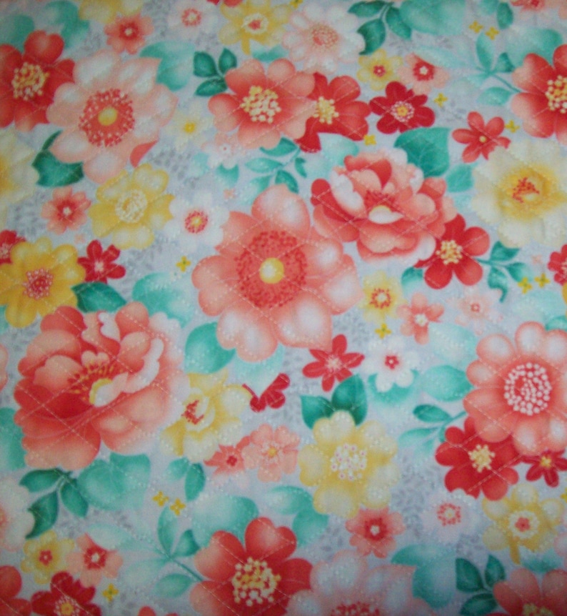 May include: Floral fabric with a quilted pattern. The design features large, coral-colored flowers with yellow centers, interspersed with smaller red and yellow blossoms. Green leaves and a light blue background complete the design.