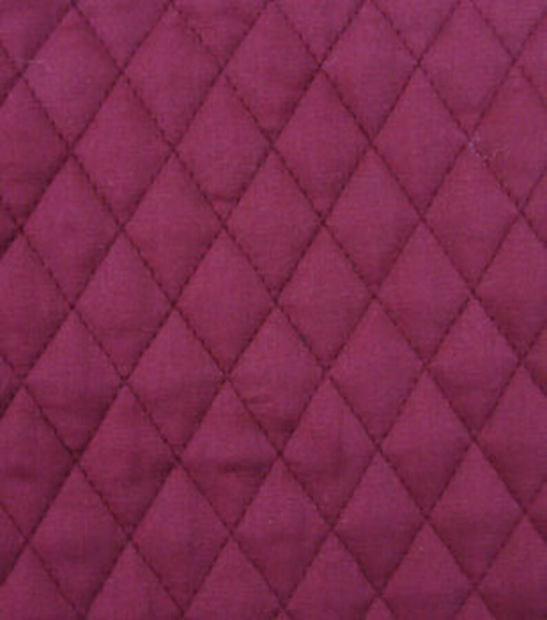 May include: Close-up of a quilted fabric with a diamond pattern. The fabric is a deep burgundy color, with visible stitching outlining each diamond. The texture appears soft and plush, suggesting a comfortable material.