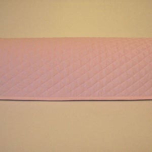 May include: A light pink quilted appliance cover. The cover is rectangular with rounded edges and a diamond pattern. The cover is designed to fit over a small kitchen appliance.