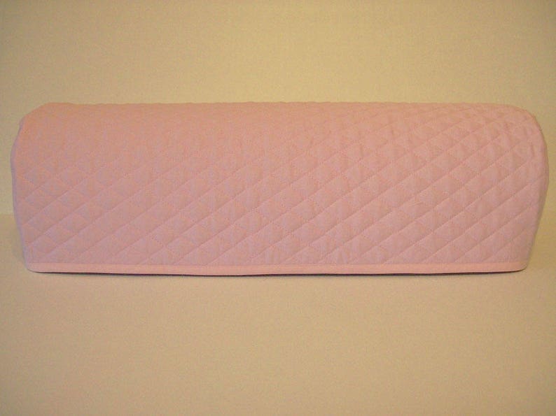 May include: A light pink quilted appliance cover. The cover is rectangular with rounded edges and a diamond pattern. The cover is designed to fit over a small kitchen appliance.