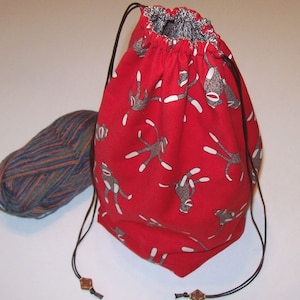 May include: Red drawstring bag with a monkey print. The bag is made of fabric and has a drawstring closure. The bag is empty.