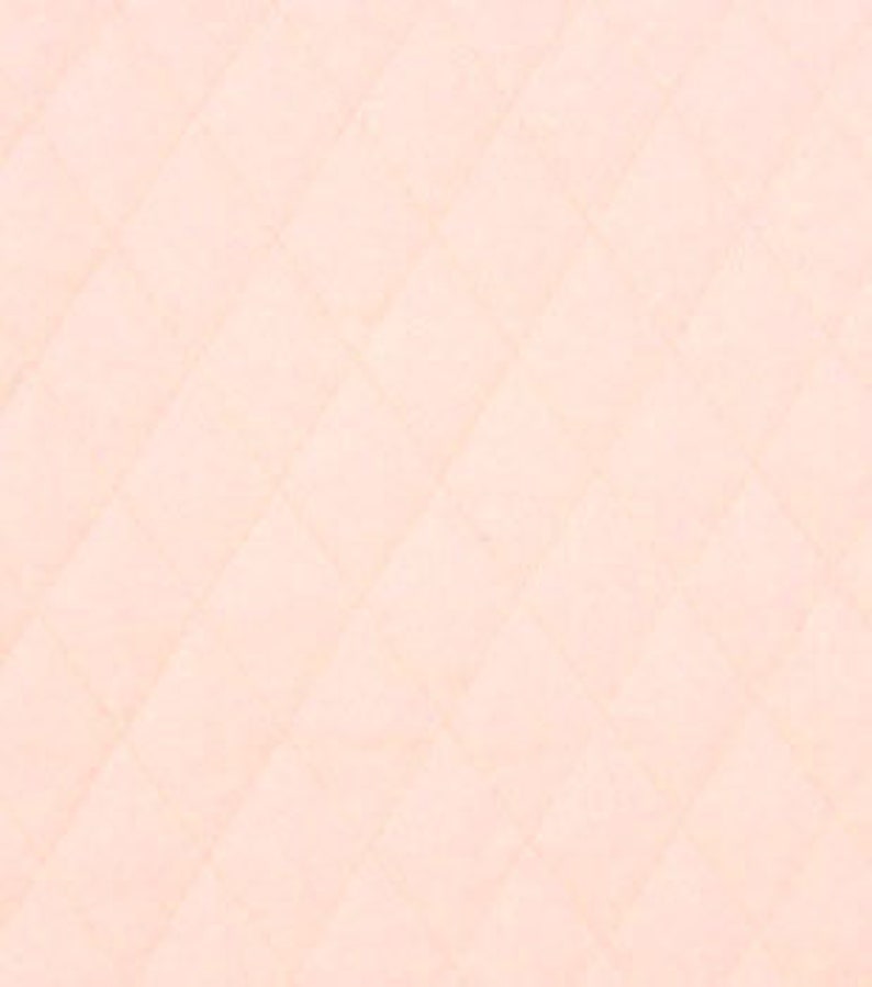 May include: A close-up of a quilted fabric in a soft peach color. The fabric has a diamond pattern created by the stitching. The texture appears smooth and slightly textured, with subtle variations in tone.
