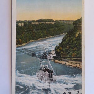 May include: A vintage postcard depicting a cable car crossing the Niagara Falls Whirlpool. The car is suspended by cables and has a large wheel at the top. The postcard is titled "Aero Cable Car Crossing the Great Whirlpool." and "Niagara Falls, Canada."