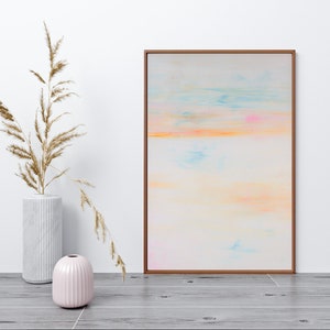 Puede incluir: Una pintura abstracta enmarcada con un fondo claro y colores pastel suaves de rosa, azul y naranja. La pintura está colgada en una pared blanca con un jarrón de hierbas secas en primer plano.
