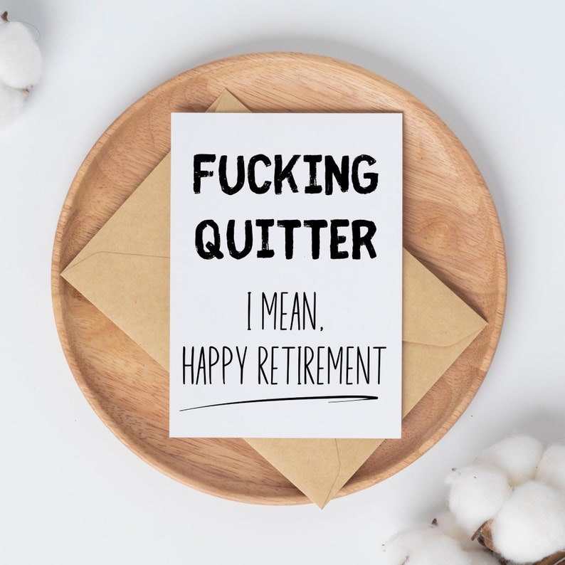 May include: A white card with black text that reads "FUCKING QUITTER I MEAN, HAPPY RETIREMENT". The card is on a wooden plate with a brown envelope.