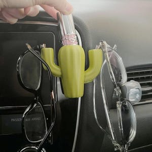 May include: A green cactus-shaped car organizer with two arms holding glasses and a lipstick tube in the center.