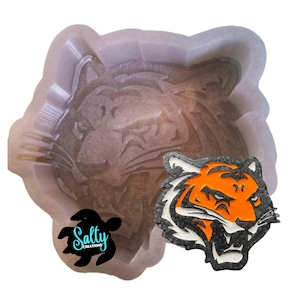 May include: A silicone mold for making resin crafts. The mold is shaped like a tiger's head. The mold is shown next to a finished resin tiger head, which is orange, black, and white.