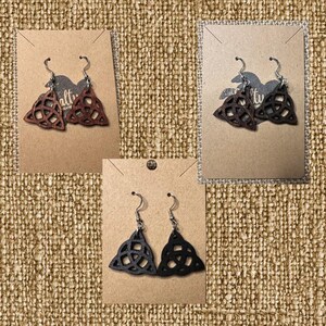 May include: Three pairs of wooden earrings with a Celtic knot design. The earrings are displayed on brown card stock with the word "alt" printed on the card. The earrings are available in black, brown, and natural wood.