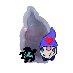 May include: A silicone mold for making a gnome with a purple hat, a red heart, and a pink nose. The mold is clear and shows the details of the gnome.
