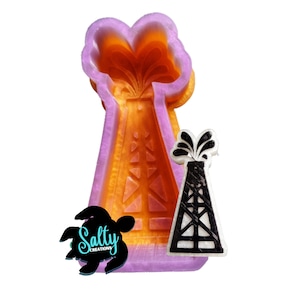 May include: Purple and orange silicone mold of an oil derrick with a black and white oil derrick silhouette. The mold is for making resin crafts.