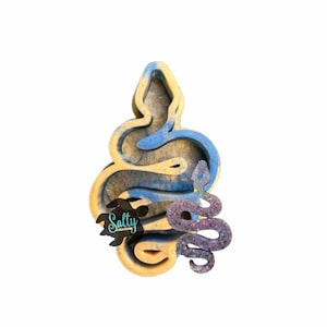May include: A blue and yellow resin snake mold with a smaller purple and iridescent glitter snake inside. The mold is shaped like a coiled snake with its head raised.