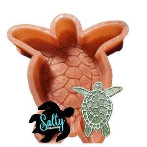May include: A brown silicone mold shaped like a turtle. The mold has a detailed texture of a turtle shell. A smaller green turtle is also pictured.