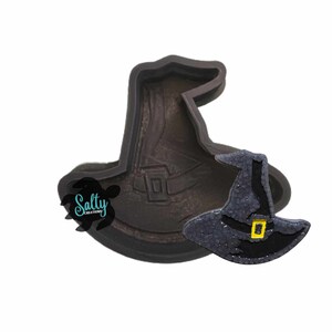 May include: A silicone mold for making witch hats. The mold is brown and has a detailed design. A small, black witch hat is shown next to the mold.