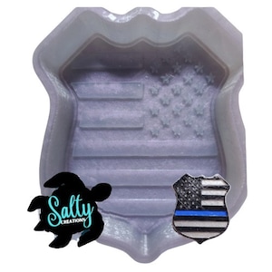 May include: A white silicone mold shaped like a police badge with an American flag design. The mold is for making resin crafts.